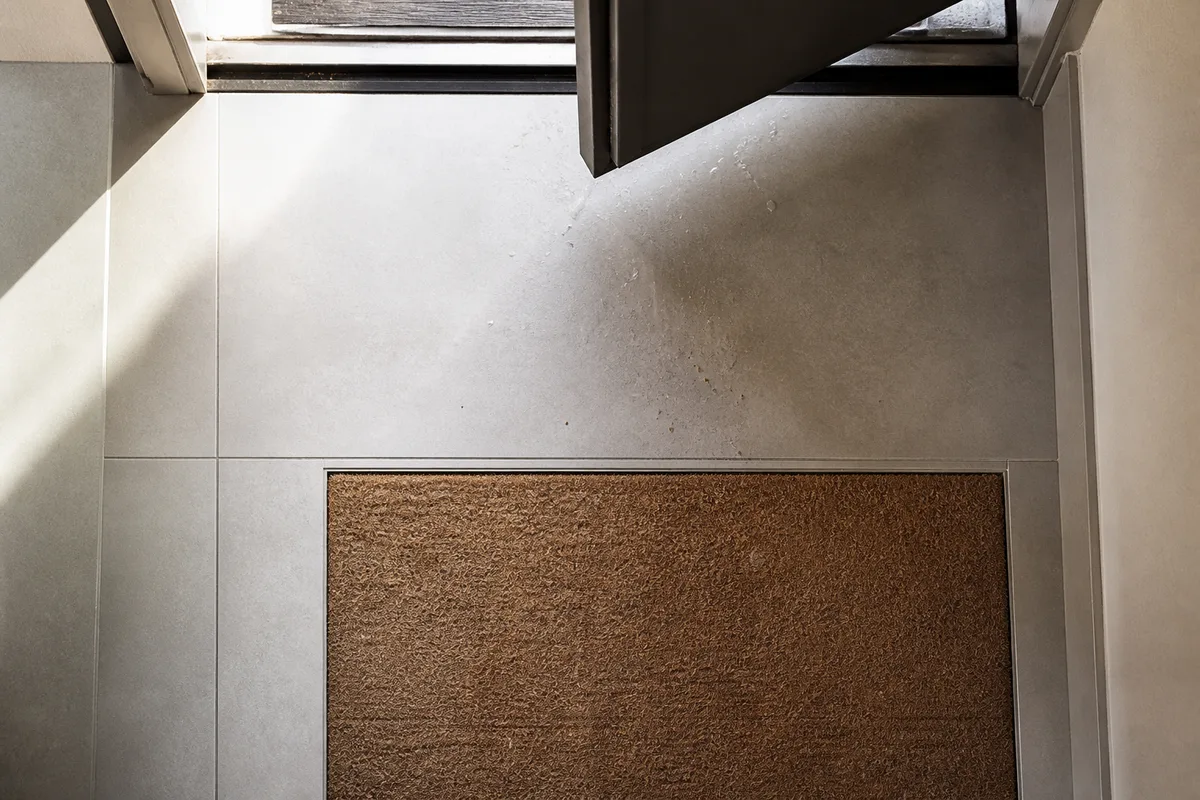 Sol en grès cérame gris avec tapis fibre encastré au seuil et lumière rasante