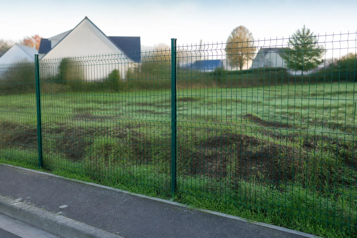 Clôture de chantier en grillage vert devant un terrain nu et herbeux